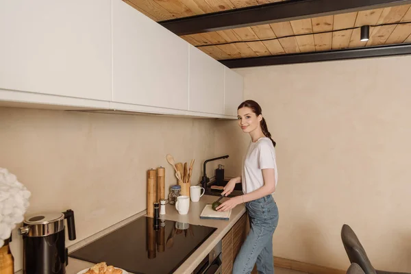 Joyeuse jeune femme coupe savoureux avocat près des tasses — Photo de stock