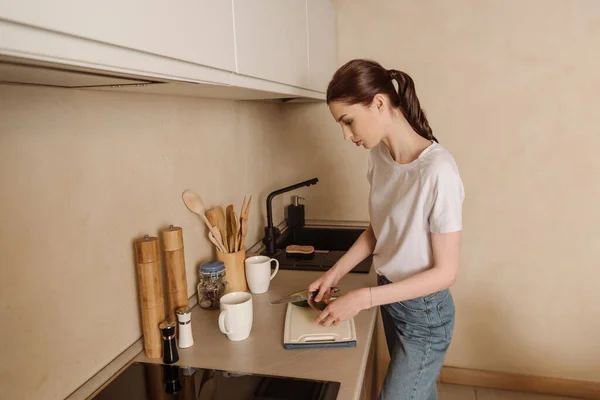 Attraktive junge Frau schneidet leckere Avocado in der Nähe von Tassen — Stockfoto