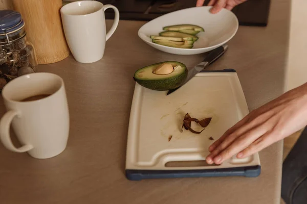 Vista recortada de la mujer de pie cerca de sabroso aguacate en la tabla de cortar — Stock Photo