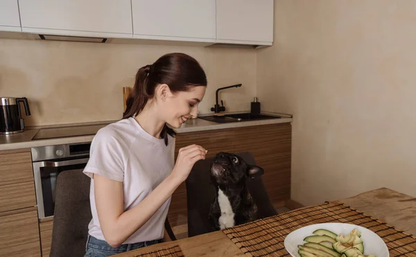 Happy young woman holding sliced avocado and looking at french bulldog — Stock Photo