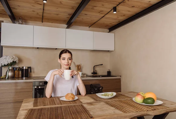 Приваблива жінка тримає чашку кави біля смачного сніданку та французького бульдога — стокове фото