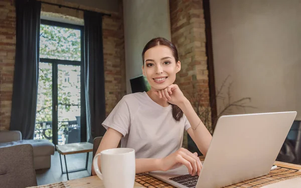 Happy freelancer looking at camera near laptop and cup of coffee — Stock Photo