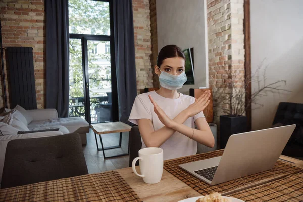 Молодий фрілансер у медичній масці, що показує знак стоп біля ноутбука — стокове фото
