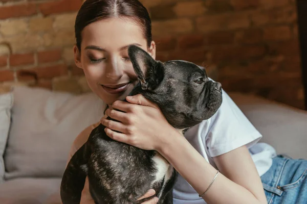 Giovane donna con gli occhi chiusi toccando bulldog nero francese a casa — Foto stock