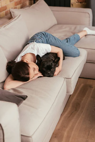 Young woman lying on sofa and touching black french bulldog — Stock Photo