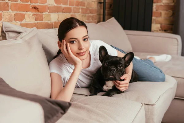 Selektiver Fokus einer jungen Frau, die mit schwarzer französischer Bulldogge auf dem Sofa liegt — Stockfoto