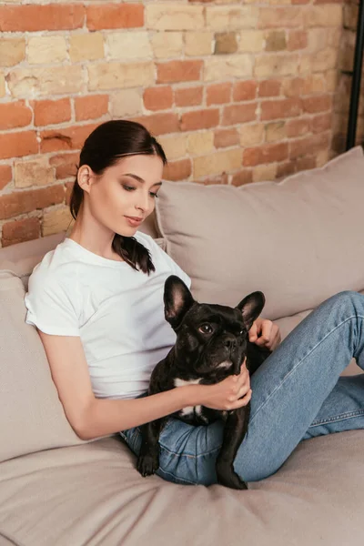 Young woman sitting on sofa with black french bulldog — Stock Photo