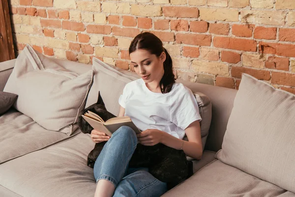 Joven mujer leyendo libro cerca negro francés bulldog - foto de stock