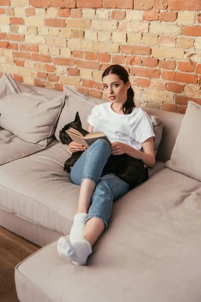 Atractiva joven sosteniendo libro cerca de bulldog francés negro - foto de stock