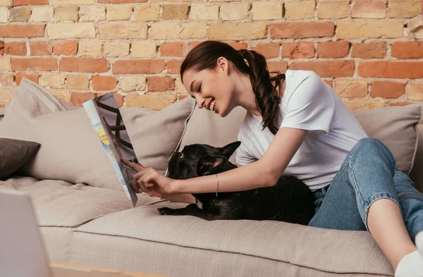 Selektiver Fokus einer glücklichen Frau beim Lesen eines Magazins in der Nähe einer schwarzen französischen Bulldogge — Stockfoto