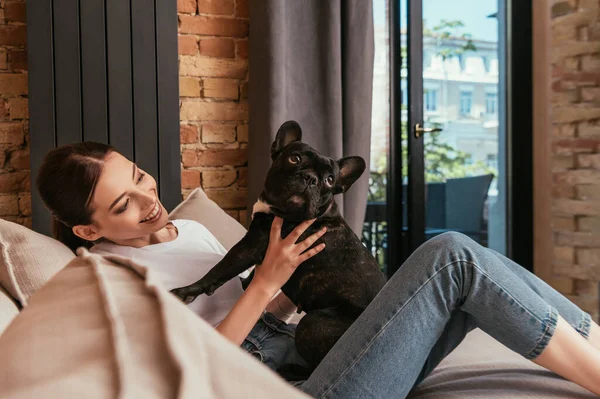 Selective focus of happy woman sitting on sofa and looking at cute french bulldog — Stock Photo