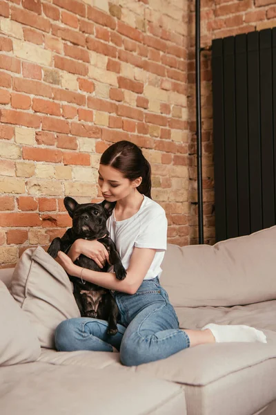 Feliz joven mujer abrazando lindo bulldog francés en sala de estar - foto de stock