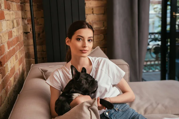 Attractive young woman holding cute french bulldog and looking at camera — Stock Photo
