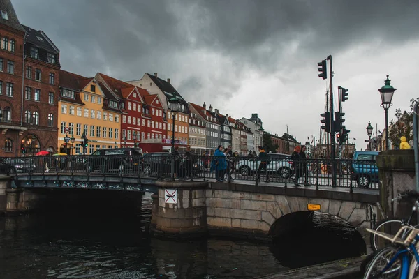 COPENHAGEN, DINAMARCA - 30 DE ABRIL DE 2020: Gente caminando por un puente cerca del canal con la calle urbana Nyhavn y el cielo nublado al fondo - foto de stock