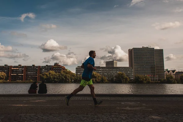 COPENHAGEN, DINAMARCA - 30 DE ABRIL DE 2020: Hombre corriendo en el paseo marítimo con canales y edificios al fondo - foto de stock