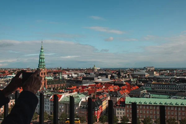 Vista recortada del hombre tomando fotos con teléfono inteligente con edificios de la ciudad de Copenhague en el fondo, Dinamarca - foto de stock