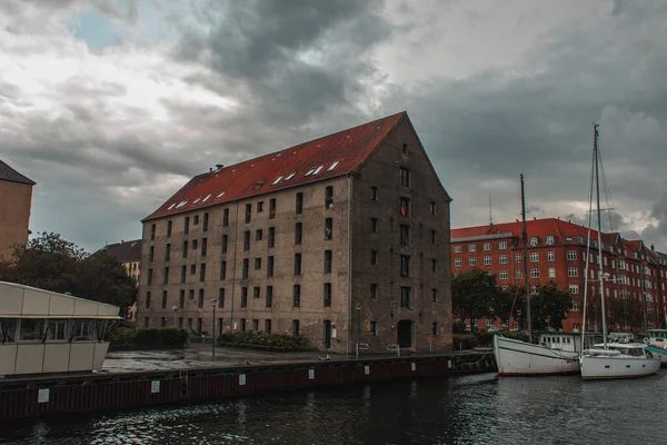 Edificios cerca del puerto y barcos en el agua con el cielo nublado en el fondo en Copenhague, Dinamarca - foto de stock