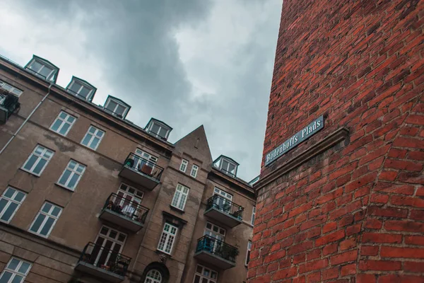 Vista de ângulo baixo de tabuleta com nome de rua na fachada de tijolo do edifício e céu nublado no fundo em Copenhague, Dinamarca — Fotografia de Stock