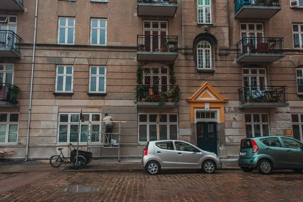 Coches en carretera cerca de la fachada del edificio en la calle urbana en Copenhague, Dinamarca - foto de stock