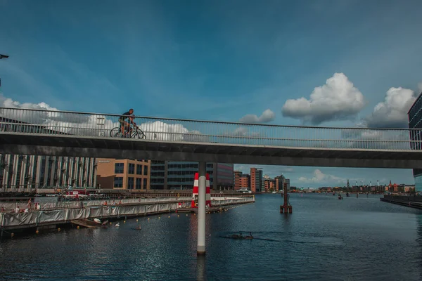COPENHAGEN, DENMARK - APRIL 30, 2020: Люди їздять мостом над річкою з міською вулицею та небом з хмарами на задньому плані. — стокове фото