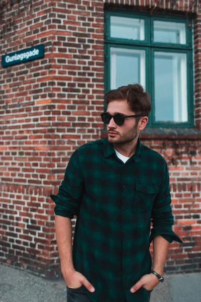 Hombre joven en gafas de sol con las manos en el bolsillo de pie en la calle urbana, Copenhague, Dinamarca - foto de stock