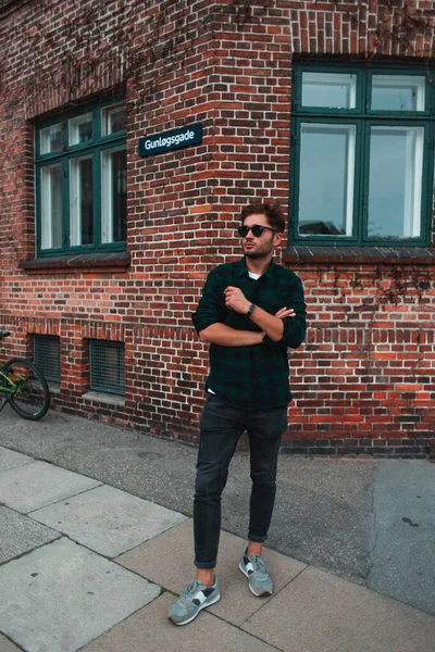 Young man in sunglasses standing near facade of building on urban street, Copenhagen, Denmark — Stock Photo