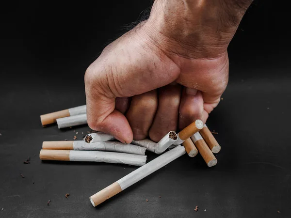 Man hand punching and destroy cigarettes on black background. Quitting smoking concept. world no tobacco day