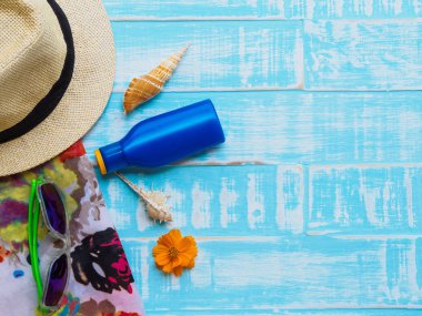 Plaj aksesuarları, güneş gözlüğü, Güneş kremi, şapka plaj da dahil olmak üzere yaz tatil ve tatil kavramı için parlak mavi ahşap arka plan üzerinde kabuk ve turuncu çiçek.