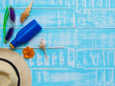 Plaj aksesuarları, güneş gözlüğü, Güneş kremi, şapka plaj da dahil olmak üzere yaz tatil ve tatil kavramı için parlak mavi ahşap arka plan üzerinde kabuk ve turuncu çiçek.