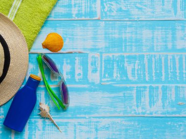Mavi plaj aksesuarları, güneş gözlüğü, Güneş kremi, şapka plaj da dahil olmak üzere deniz hayvanı kabuğu ve parlak yeşil havluda yaz tatil ve tatil kavramı için ahşap arka plan.