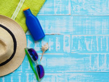 Mavi plaj aksesuarları, güneş gözlüğü, Güneş kremi, şapka plaj da dahil olmak üzere deniz hayvanı kabuğu ve parlak yeşil havluda yaz tatil ve tatil kavramı için ahşap arka plan.