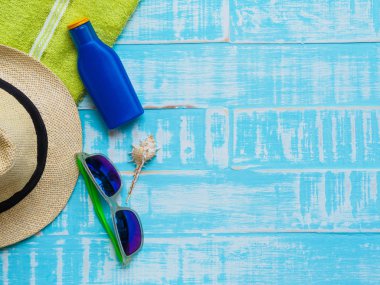 Mavi plaj aksesuarları, güneş gözlüğü, Güneş kremi, şapka plaj da dahil olmak üzere deniz hayvanı kabuğu ve parlak yeşil havluda yaz tatil ve tatil kavramı için ahşap arka plan.