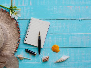 Plaj aksesuarları çiçekler, şapka plaj, kabuk da dahil olmak üzere, Not defteri ve kalem üzerinde parlak pastel ahşap arka plan için yaz tatil ve tatil kavramı mavi.