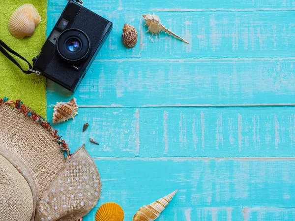 Plaj aksesuarları, şapka beach de dahil olmak üzere deniz hayvanı kabuğu, havlu ve retro kamera üzerinde parlak mavi yaz tatil ve tatil kavramı için ahşap arka plan.