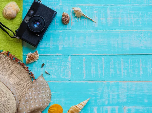 Plaj aksesuarları, şapka beach de dahil olmak üzere deniz hayvanı kabuğu, havlu ve retro kamera üzerinde parlak mavi yaz tatil ve tatil kavramı için ahşap arka plan.