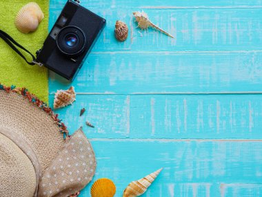 Plaj aksesuarları, şapka beach de dahil olmak üzere deniz hayvanı kabuğu, havlu ve retro kamera üzerinde parlak mavi yaz tatil ve tatil kavramı için ahşap arka plan.