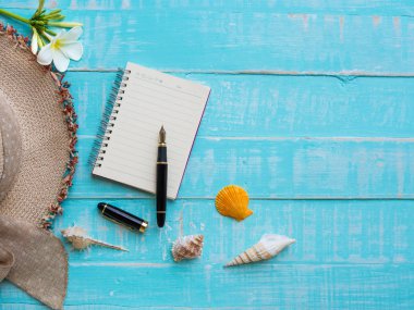 Plaj aksesuarları çiçekler, şapka plaj, kabuk da dahil olmak üzere, Not defteri ve kalem üzerinde parlak pastel ahşap arka plan için yaz tatil ve tatil kavramı mavi.