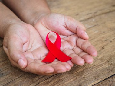 Sağlık ve tıp kavramı - ahşap arka plan üzerinde kırmızı AIDS bilinçlendirme şerit tutan eller. Dünya AIDS Günü.