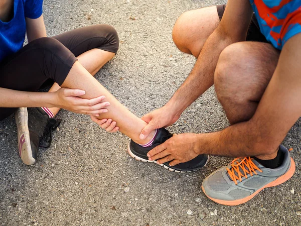 Ankle sprained. Young woman suffering from an ankle injury while exercising and running and she getting help from man touching her ankle. Healthcare and sport concept.