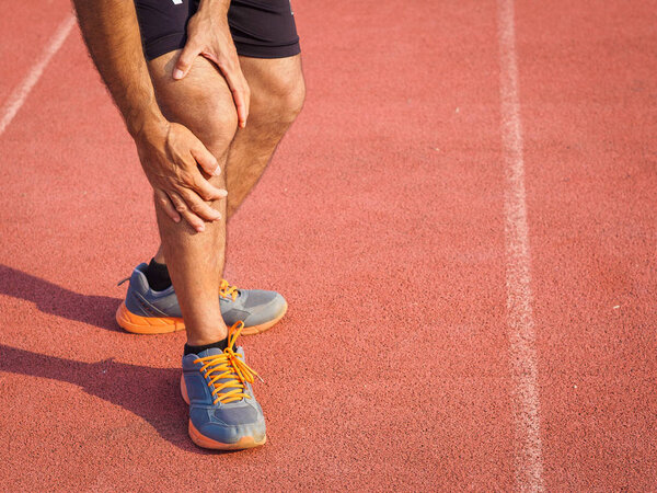 knee Injuries. sport man with strong athletic legs holding knee with his hands in pain after suffering muscle injury during a running workout training on Running Track. Healthcare and sport concept.