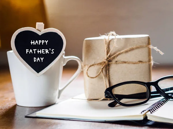 Happy fathers day concept. coffee cup with gift box, heart tag with HAPPY FATHER\'S DAY text, notebook and glasses on wooden table background.