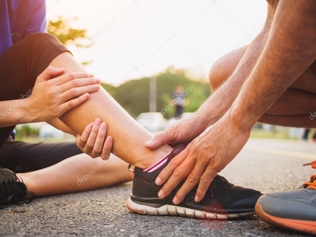 Ankle sprained. Young woman suffering from an ankle injury while exercising and running and she getting help from man touching her ankle. Healthcare and sport concept.