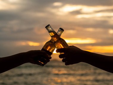Bira şişesi tutarak ve gün batımı sahilde duyulmamasını çift eller. Parti, tatil, yaz, dostluk kavramı.