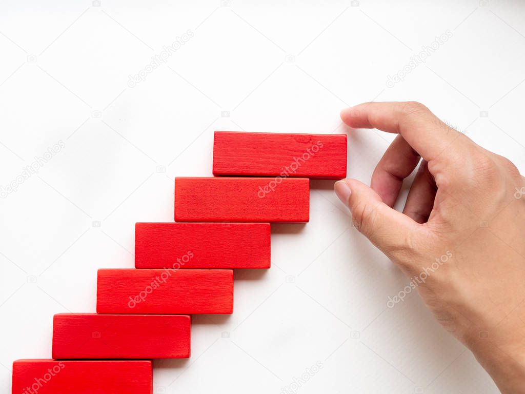 Concept of building success foundation. Women hand put red wooden block in the shape of a staircase