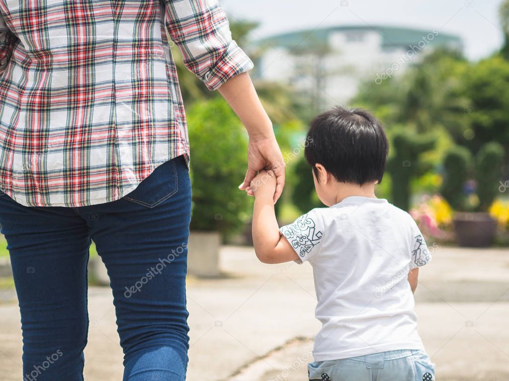 Mother and daughter holding hands walking in the park. Kid and Mom Family Concept.