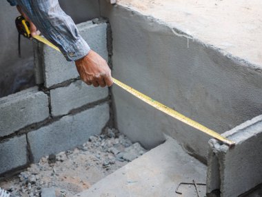 Profesyonel inşaat işçisi ölçü ve döşeme tuğla çimento ile ölçüm bandı kullanır.