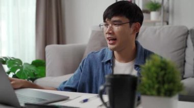 Günlük kıyafetler giyen, dizüstü bilgisayarla çalışan, akıllı telefon, hesap makinesi olan, evdeki oturma odasındaki kanepede oturan, ev konseptiyle çalışan bir adam..