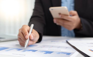 Finans işadamları, müşteriler, Vergi ve muhasebe sistemi konseptine sunum hazırlamak için şirketin mali performansı hakkındaki verileri hesaplamak ve analiz etmek için cep telefonlarını kullanırlar..