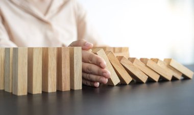 İş kadını sürekli risk almak, sürekli hasar azaltmak, iş dominosu başarısızlıklarını durdurmak için domino taşının üzerine düşen elleri durdurur..