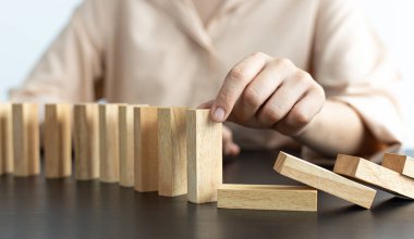 İş kadını sürekli risk almak, sürekli hasar azaltmak, iş dominosu başarısızlıklarını durdurmak için domino taşının üzerine düşen elleri durdurur..